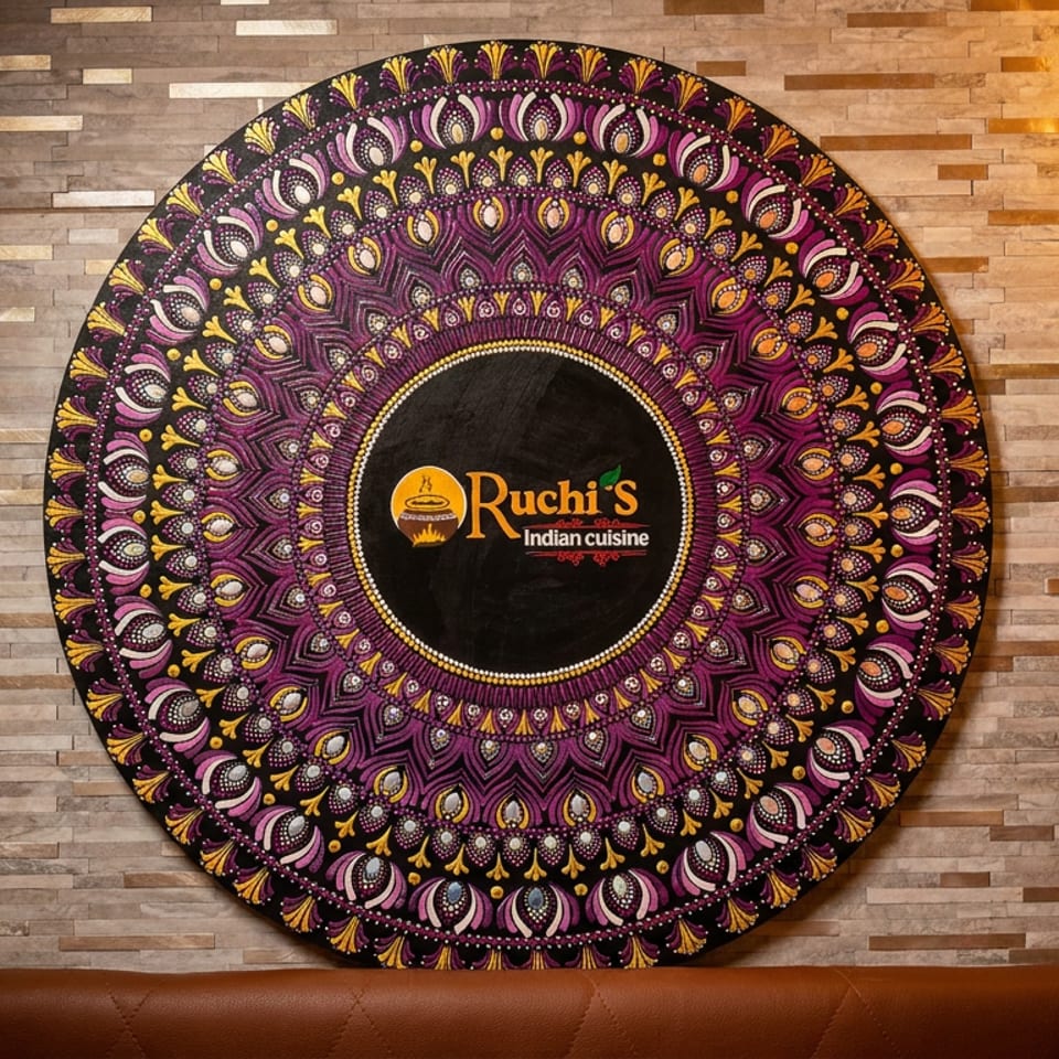 Ruchi's Indian Cuisine logo on a large, ornate purple and gold mandala against a stone wall.
